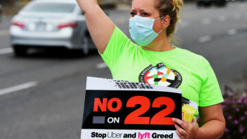 A Rideshare driver shouts to drivers while holding up a sign that reads "No on 22"