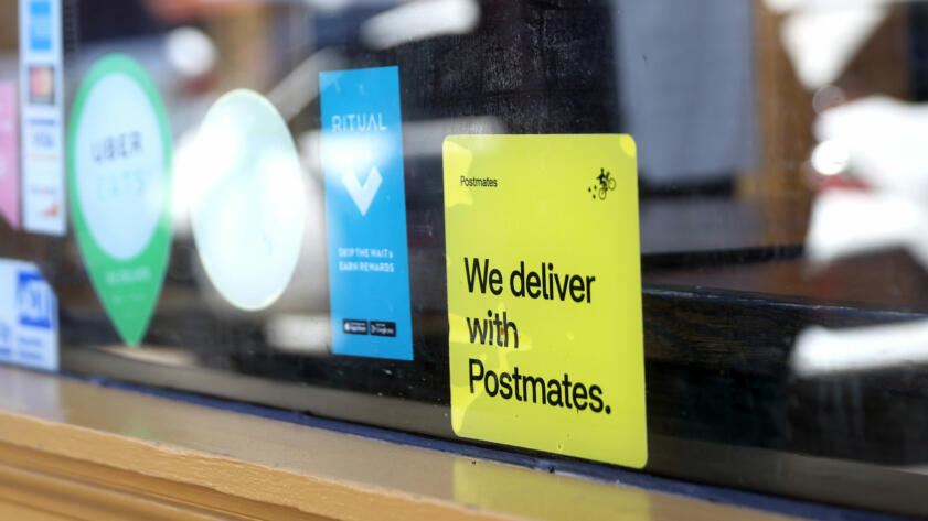 A photo of a 'We deliver with Postmates' sticker in the window of a restaurant in San Francisco