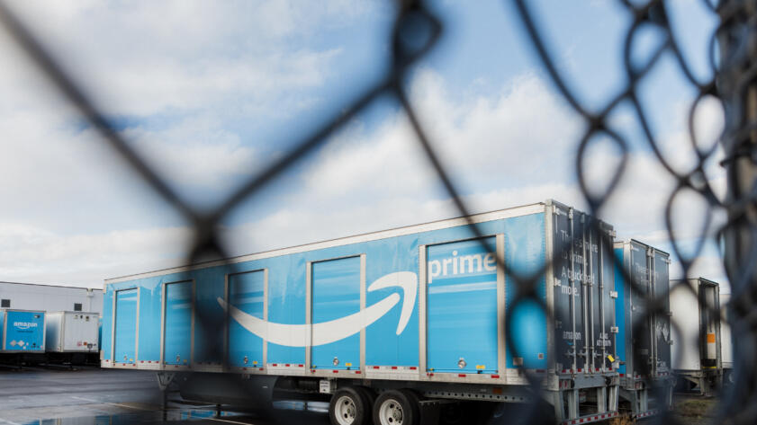 A blue Amazon prime truck framed behind a wire fence.
