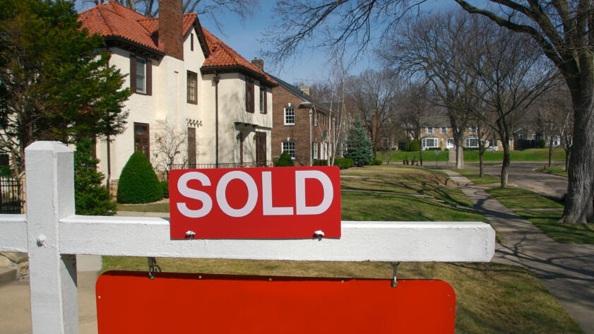 Red sold sign in the foreground. Houses in the background.