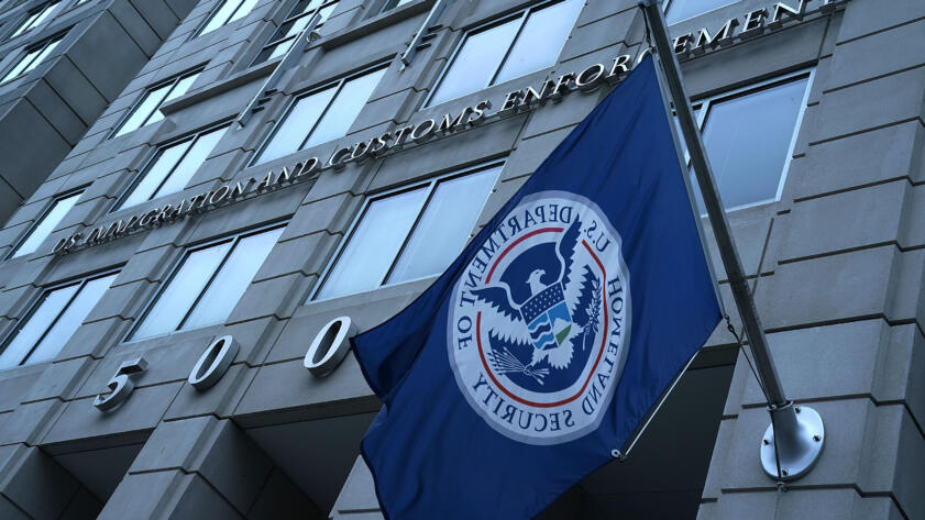 Photo looking upward at ICE building in Washington, D.C., with Homeland Security flag in foreground