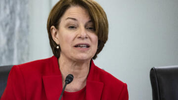 Photo of Amy Klobuchar in red suit before a microphone