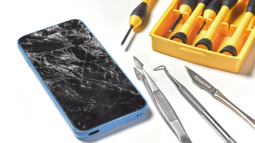 Image of a phone with a broken screen and various tools next to it