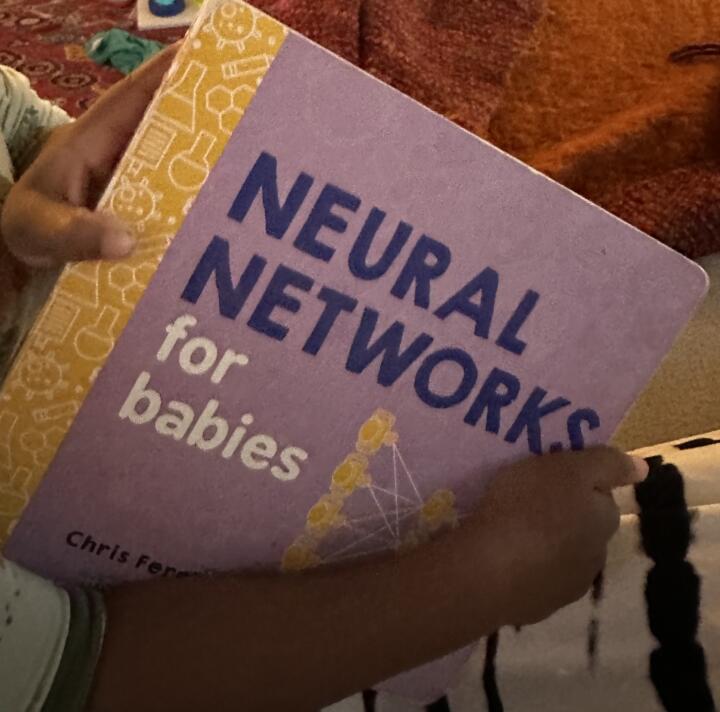A photograph of a child's hands holding a book with the title "Neural Networks for babies."