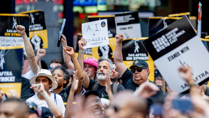 Photograph of a protester holds a sign that reads "AI is Soulless" in a crowd of other people with their fists raised and holding signs.