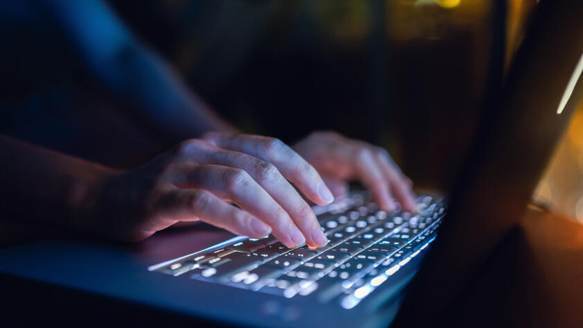 Photograph of a closeup of hands typing on a laptop.