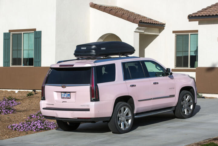 Photograph of a pink Mary Kay Cadillac Escalade parked in the driveway of a home.