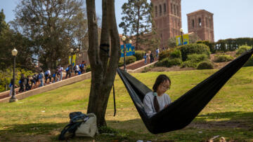 Photograph of an Asian student with glasses sitting in a hammock. Behind her, there's a line of young people walking up the stairs on the UCLA campus.