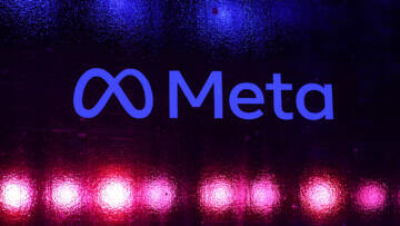 Photograph of the Meta logo on a glass window backlit by red and blue light.