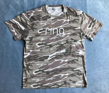 Photograph of the front of a Ring shirt laid out on a flat surface, with the Ring logo printed over a camouflage pattern.