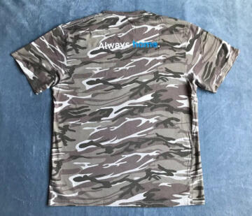 Photograph of the back of a Ring shirt laid out on a flat surface, with the words “Always home” printed over a camouflage pattern.