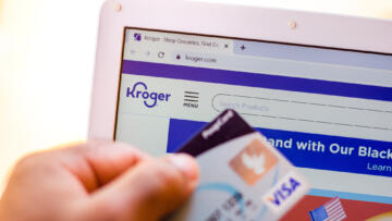 A person holding a credit card as they visit Kroger's website