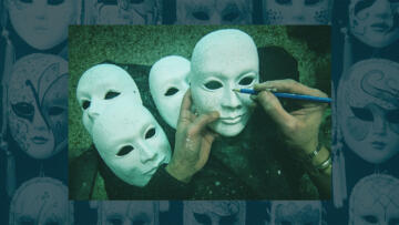 A person's hands hold a pencil and a white mask. Three other white masks sit in the background.