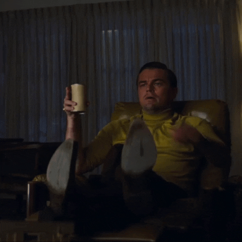 Animated GIF of a seated Leonardo DiCaprio in Once Upon a Time in Hollywood leaning forward on the edge of his seat and pointing