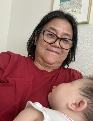 Photo of Bùi smiling while holding her baby grandchild, who is sleeping