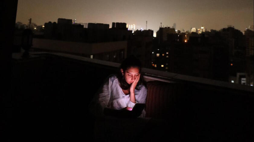 Photograph of Mirna El Helbawi looking down at her phone on a rooftop at night