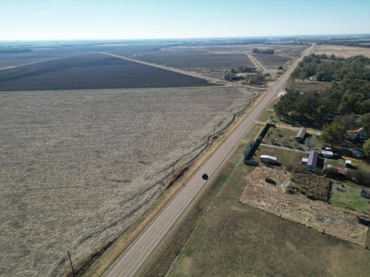 Aerial drone shot of Rome, Miss., showing a car driving on a main road passing mostly sparse fields