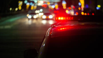 Photograph focusing on the back of police car lights at night, with blurred cars facing the other direction in the background