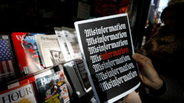 Photograph of a hand holding a magazine at a newstand; the cover features the word misinformation repeated several times in a gothic typeface