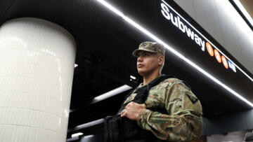 Low-angle photograph of a National Guard soldier in front of a New York City subway sign