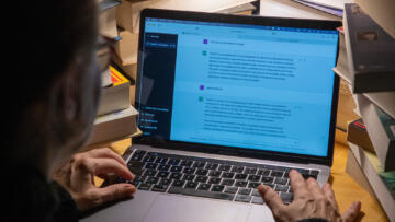 Over-the-shoulder photo of a person using a laptop displaying a ChatGPT conversation