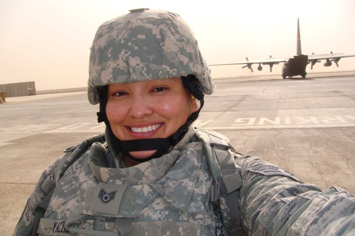 A woman in camouflage gear takes a selfie with a plane in the background