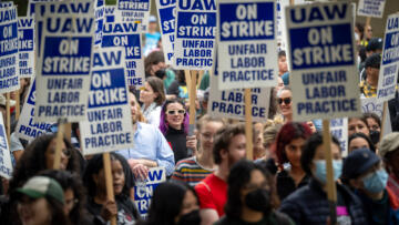 Wide-shot photograph of a crowd of unionized academic workers holding signs that say “UAW on Strike Unfair Labor Practice”