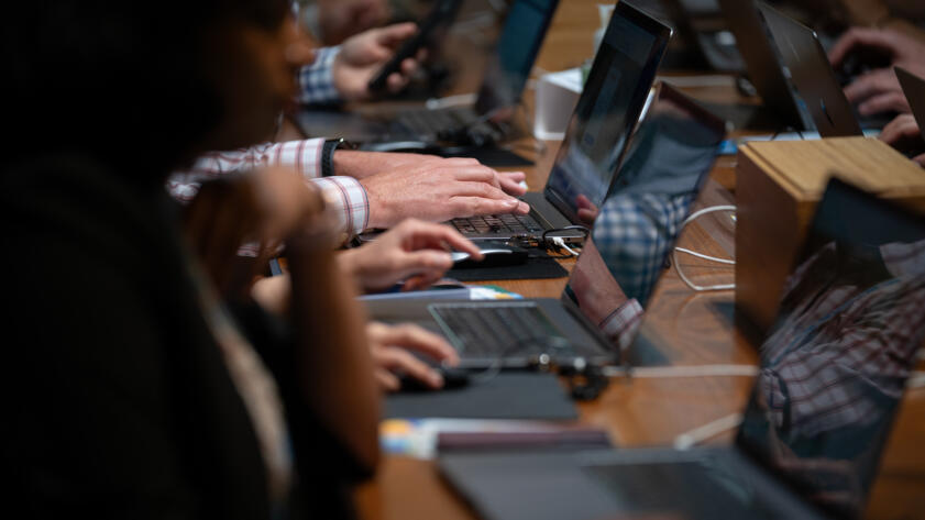 A close-up view of people's hands typing or scrolling on their laptops at an event.