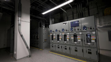 A white room with power cords throughout the ceiling leading to machinery with transfer switches in a data center. White fluorescents light up most of the room, with shadows in the background between the machinery.