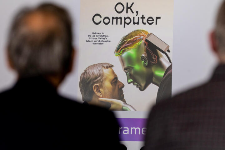 Two people in the foreground observe a large poster titled "OK, Computer," featuring an illustration of a human and a green-skinned humanoid figure with exposed circuitry staring intently at each other. The humanoid has a device attached to its head, suggesting a connection to artificial intelligence. The text on the poster references the AI revolution and Silicon Valley’s latest technological advancements. The image is framed in a dimly lit setting, with the focus on the futuristic artwork.