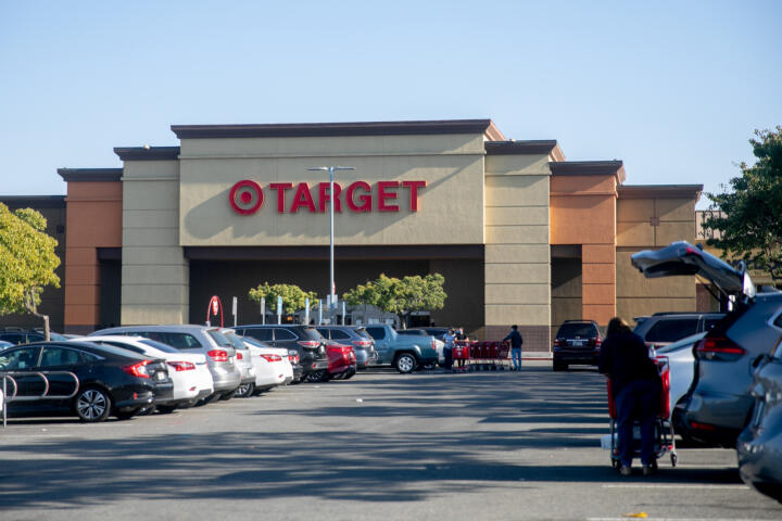 An beige and orange colored building with the words "Target" in front of it, as seen from a parking lot filled with cars and some shoppers.