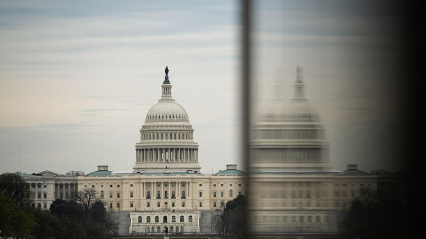 A view of the dome-structure of the U.S. Capitol in Washington D.C. taken and next to its blurry reflection on a glass wall in the foreground.