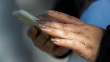 A close-up view of a person holding a white cell phone with both their hands. A ray of light softly illuminates the person's left hand.