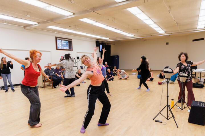 A group of students inside a dance studio, posing in different dance positions while a practice is taking place.